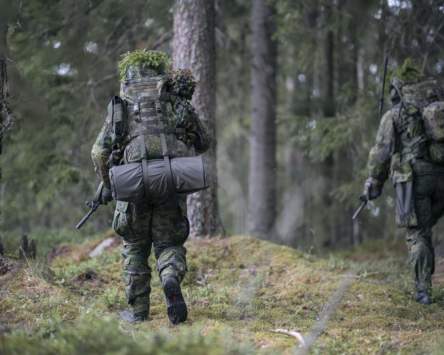 Ein Soldat mit Rucksack und befestigter zusammengerollter Isomatte, der durch den Wald streift. 