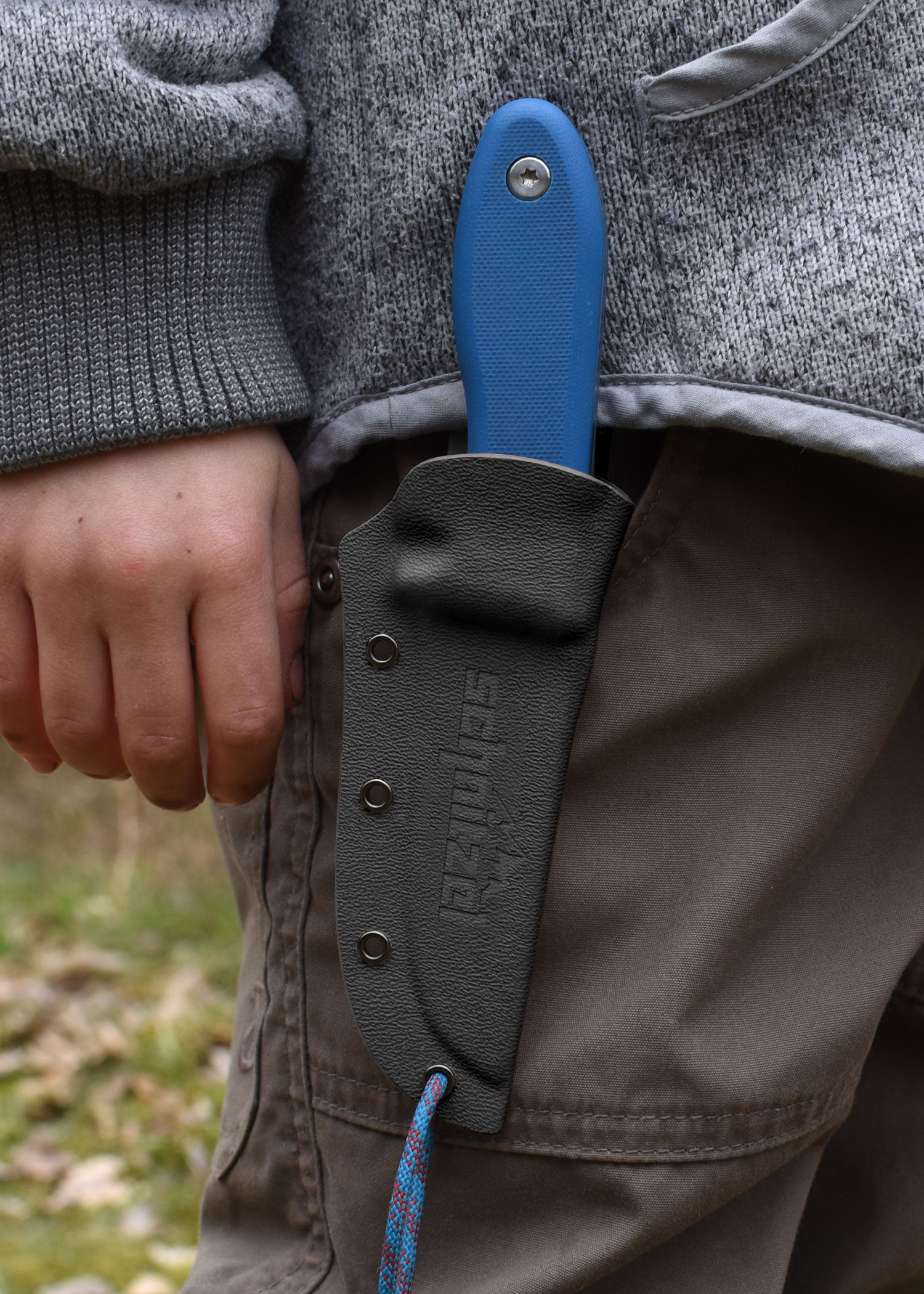 Das Kinderschnitzmesser UNU blau an einer Hose befestigt.